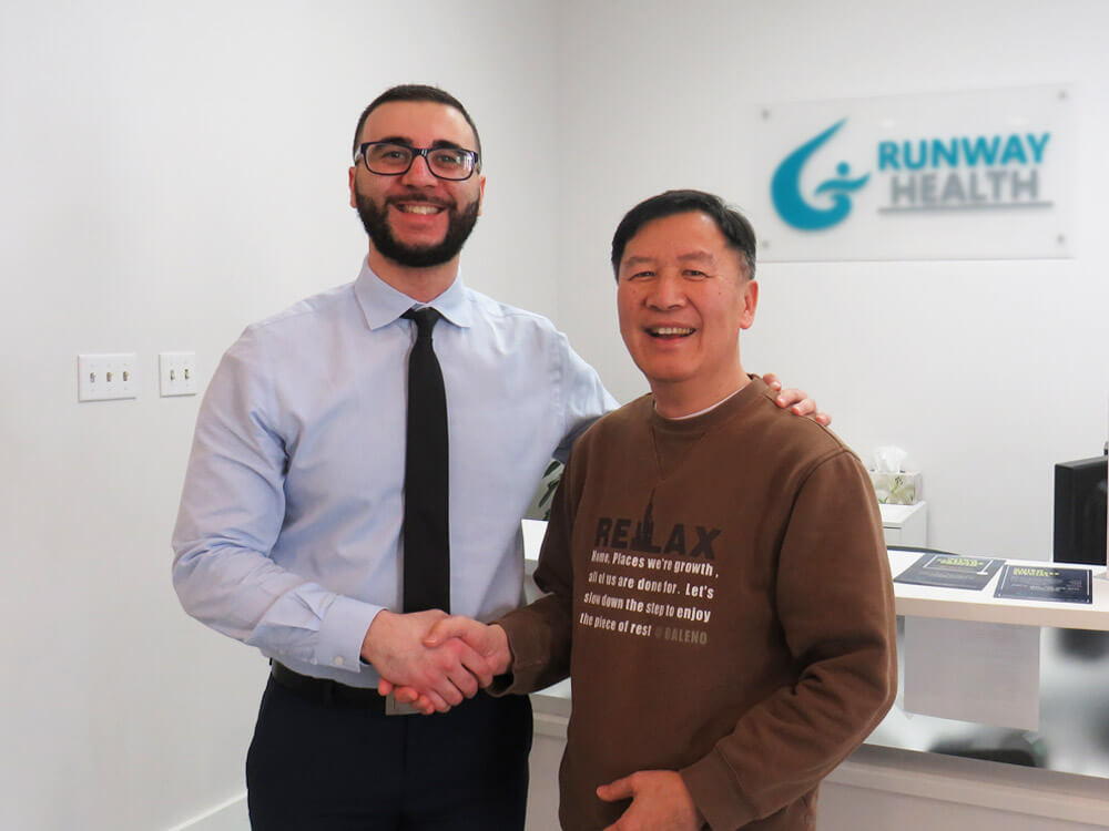 Dr. Omar, a chiropractor, is in reception shaking hands with Raymond, a long-time patient of the clinic.