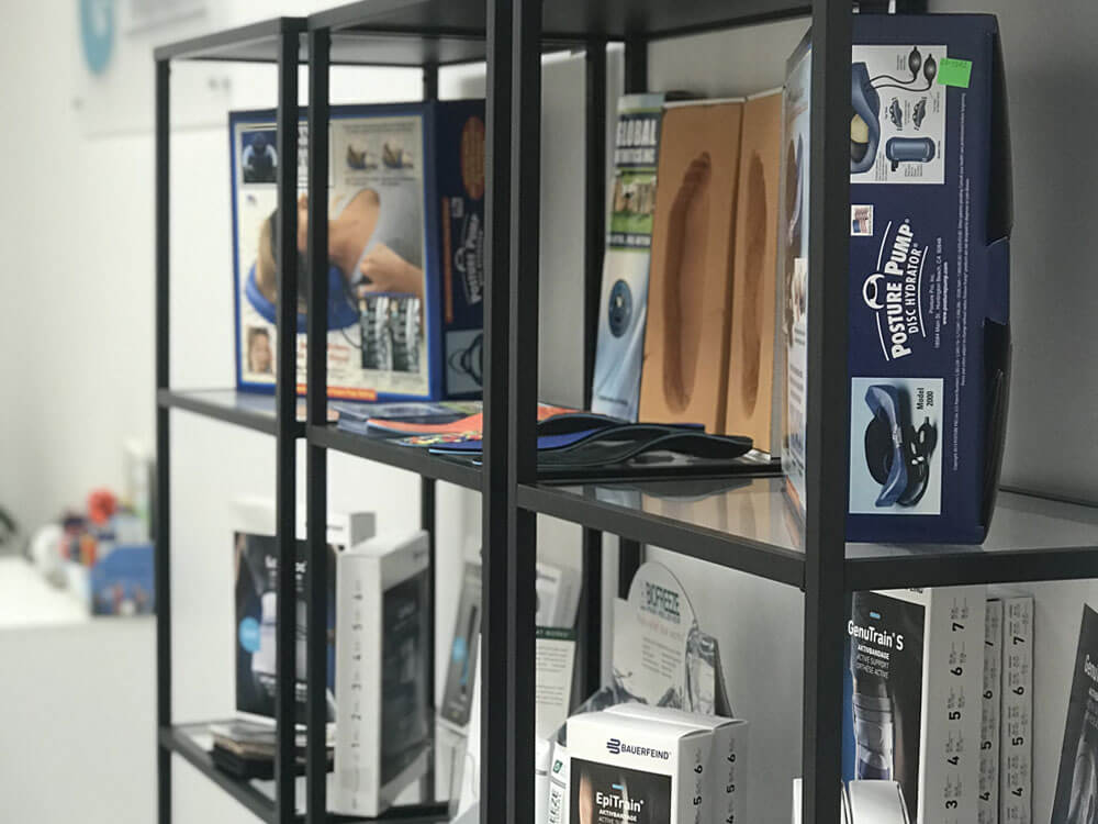 An angled view of the product display shelf in reception at Runway Health. Products include custom-made orthotics, compression stockings, orthoapedic knee and low back braces, and biofreeze.