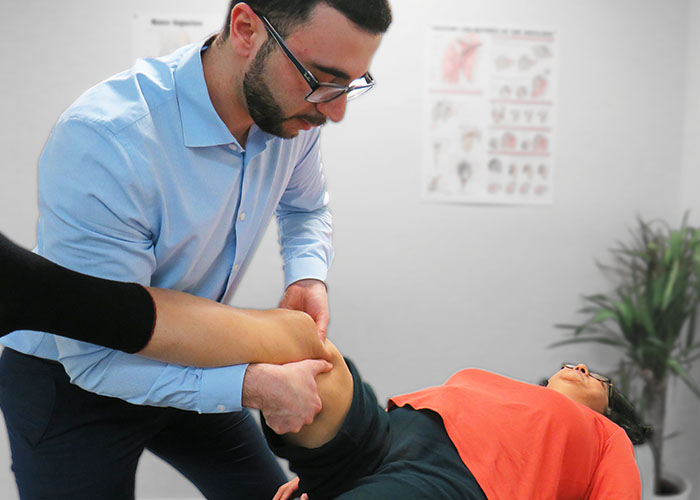 Dr. Omar, a chiropractor, performing advanced manual therapy for muscles around the knee of a patient dealing with osteoarthritis of the right knee. The patient is laying on their back while Dr. Omar has the leg lifted and slightly bent while applying pressure to specific muscles.