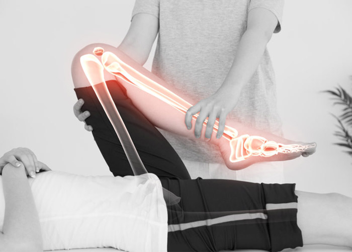 A physiotherapist assessing the knee of a patient by bending it maximally while the patient is laying on their back. The anatomy of the skeletal bones is shown through the skin to understand the anatomy of the knee.