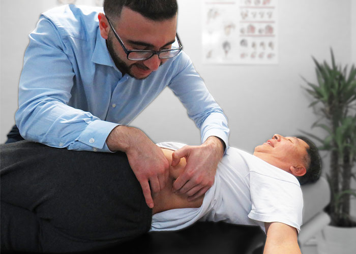 Dr. Omar, a chiropractor, performing soft-tissue therapy and manual release of muscular in the low back of a patient who is laying on their side on a chiropractic table.