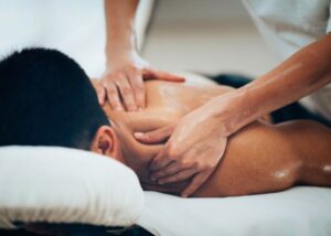 A massage therapist doing deep tissue release on the shoulder of a patient who is laying on their back. This can help circulation, increase range of motion, provide pain relief, and improve posture.