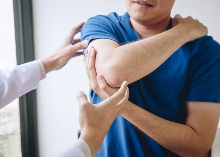 A physiotherapist assessing the right shoulder of a male patient. The patient's right arm is being stretches across his chest.