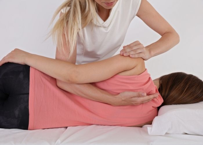 A female physiotherapist is performing mobilizations on the left shoulder of a female patient. This helps increase range of motion in the shoulder