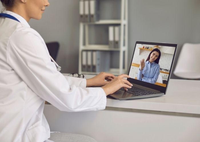 Young woman in white lab coat hosting a virtual consultation on her laptop