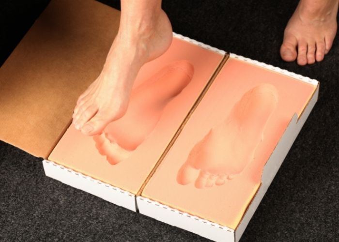 A patient putting their foot into a 3D volumetric foam cast box. This is one of the ways to take a mold of the foot to create custom orthotics.