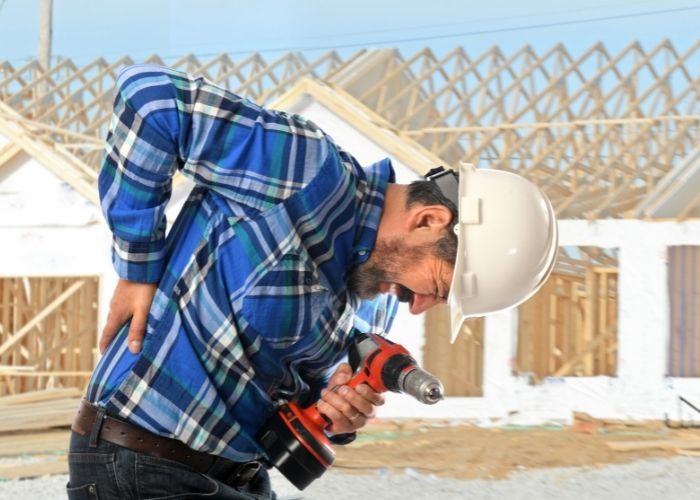 a construction working grasping to his low back and wincing in pain due to a workplace accident injury.