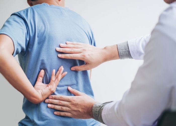 A physiotherapist assessing a patient's lower back while the patient is pointing to the painful area.