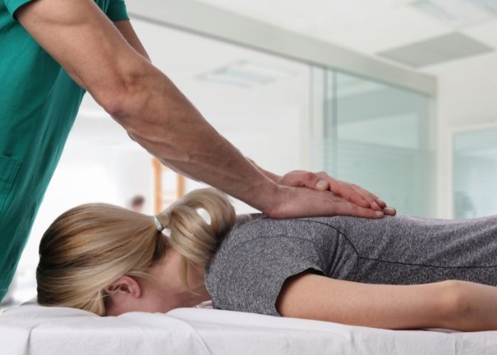 A male physiotherapist applying pressure to a male patient's mid-back while she is laying on her stomach.