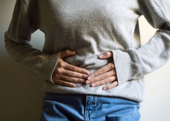 A woman holding her stomach due to menstrual pain during an examination with a pelvic health physiotherapist.